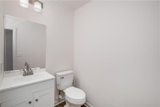 half bath featuring baseboards, vanity, and toilet