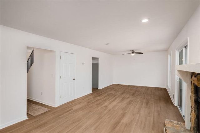 unfurnished living room with recessed lighting, light wood-style floors, ceiling fan, a stone fireplace, and baseboards