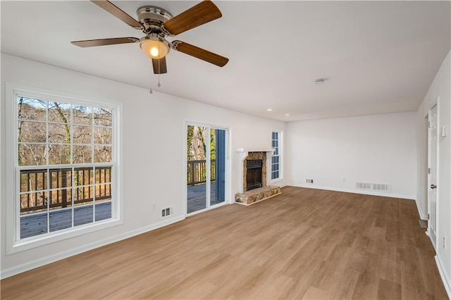 unfurnished living room featuring a stone fireplace, wood finished floors, visible vents, and baseboards