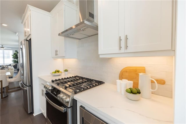 kitchen with dark wood-type flooring, wall chimney range hood, light stone countertops, appliances with stainless steel finishes, and white cabinetry