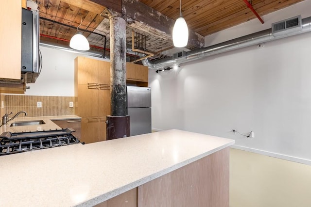 kitchen featuring a sink, pendant lighting, backsplash, visible vents, and freestanding refrigerator
