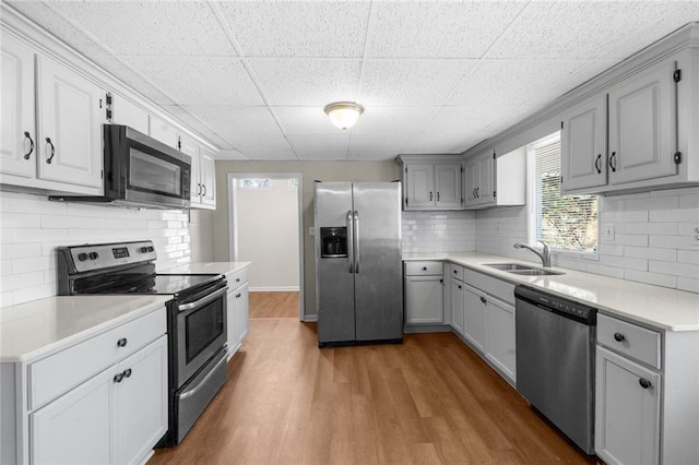 kitchen with gray cabinetry, a sink, wood finished floors, stainless steel appliances, and light countertops