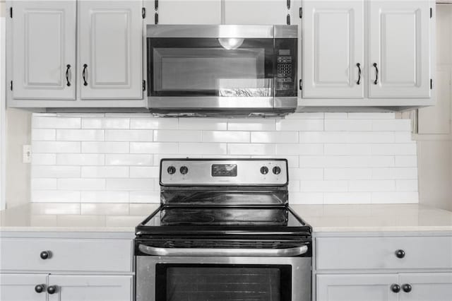 kitchen with tasteful backsplash, appliances with stainless steel finishes, white cabinetry, and light countertops