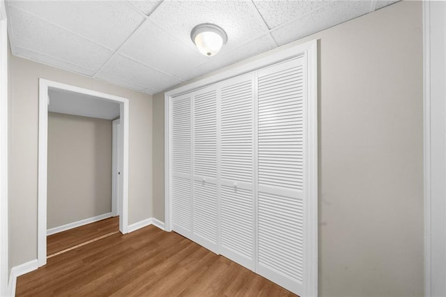 interior space with a drop ceiling, baseboards, and wood finished floors