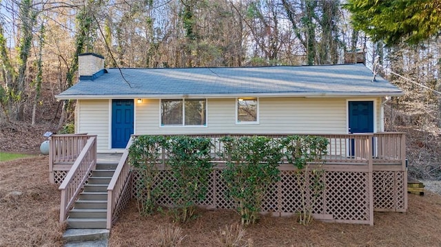 view of front of house featuring a wooden deck, a chimney, stairs, and a shingled roof