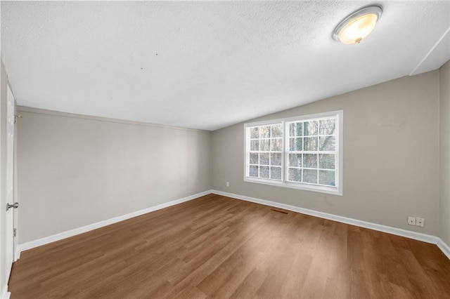 spare room with wood finished floors, a textured ceiling, baseboards, and vaulted ceiling