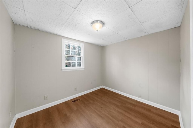 empty room with dark wood finished floors, visible vents, baseboards, and a drop ceiling