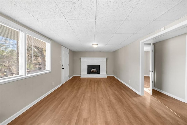 unfurnished living room featuring a drop ceiling, a fireplace, baseboards, and wood finished floors