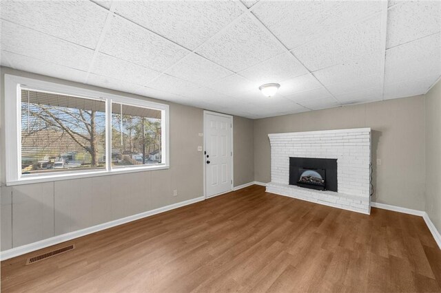 unfurnished living room featuring visible vents, a drop ceiling, wood finished floors, a fireplace, and baseboards