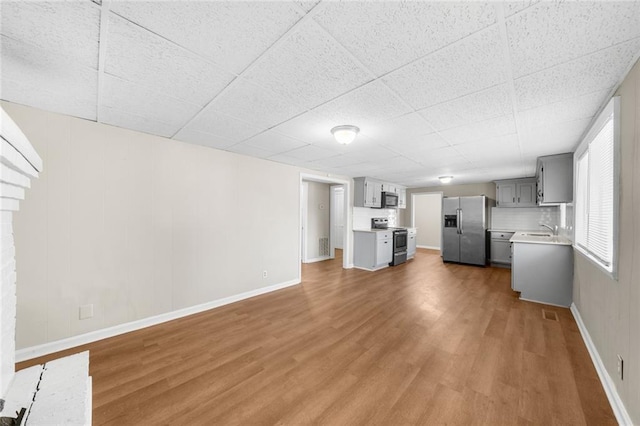 unfurnished living room featuring a sink, baseboards, and wood finished floors