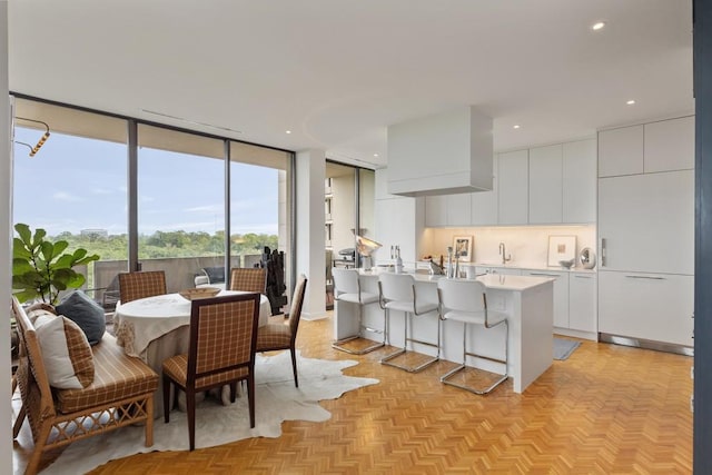 kitchen featuring a center island with sink, a kitchen breakfast bar, light parquet floors, and white cabinets