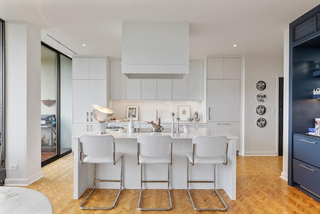 kitchen featuring white cabinetry, a kitchen island with sink, a breakfast bar area, and light parquet flooring