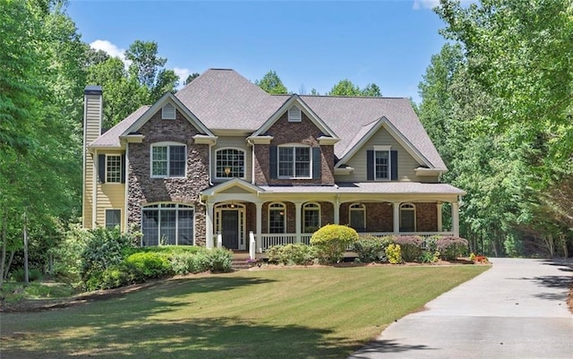 craftsman-style home featuring a porch, a chimney, a front yard, and stone siding