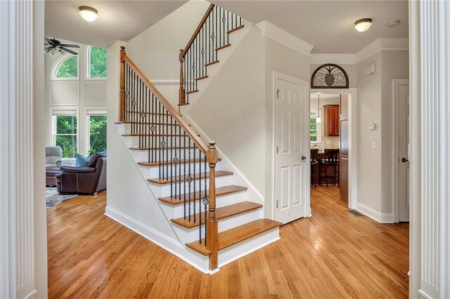 stairs with a ceiling fan, wood finished floors, healthy amount of natural light, and ornamental molding