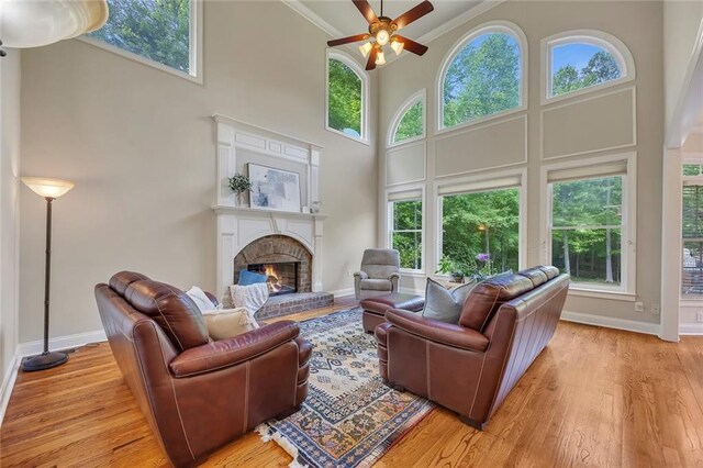 living room featuring a ceiling fan, a high ceiling, light wood finished floors, a brick fireplace, and ornamental molding