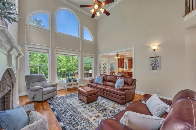 living area with ceiling fan, a fireplace, crown molding, a high ceiling, and baseboards