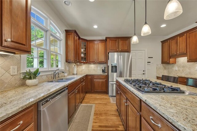kitchen with appliances with stainless steel finishes, a sink, backsplash, ornamental molding, and light stone counters