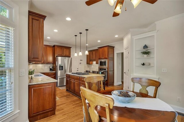 kitchen featuring stainless steel appliances, ceiling fan, crown molding, a sink, and a kitchen island