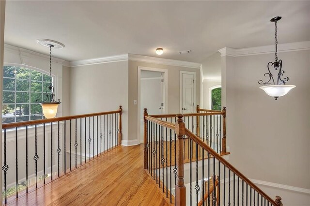 hallway with light wood-type flooring, an upstairs landing, ornamental molding, and baseboards