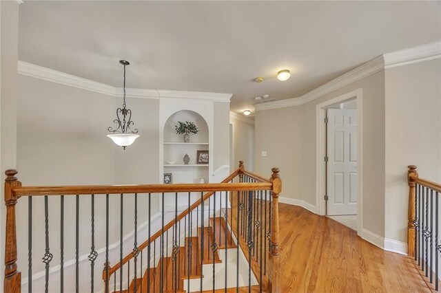 hallway with an upstairs landing, crown molding, light wood-style flooring, baseboards, and built in features