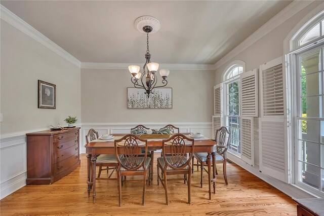 dining room with healthy amount of natural light, a chandelier, ornamental molding, light wood-type flooring, and a wainscoted wall
