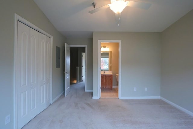 unfurnished bedroom with ceiling fan, electric panel, ensuite bathroom, light colored carpet, and a closet