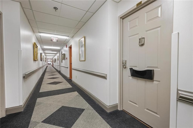 hall featuring a drop ceiling and baseboards