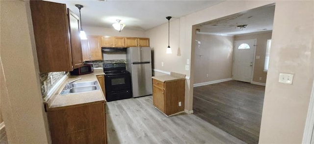 kitchen with hanging light fixtures, black appliances, light wood-type flooring, and sink