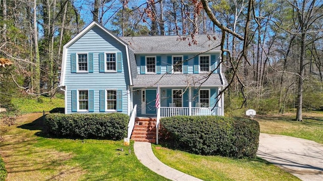 view of front of home featuring covered porch, a shingled roof, and a front lawn