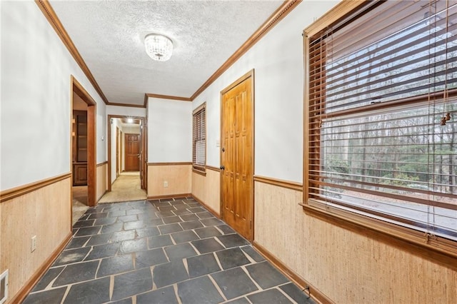 corridor featuring a wealth of natural light, a textured ceiling, wood walls, and wainscoting