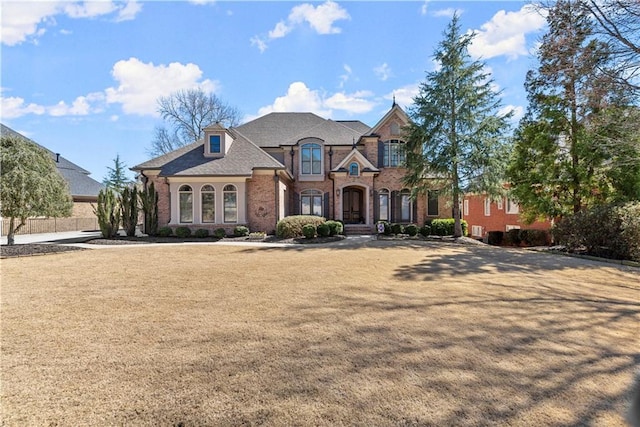 french country home featuring a front lawn and brick siding