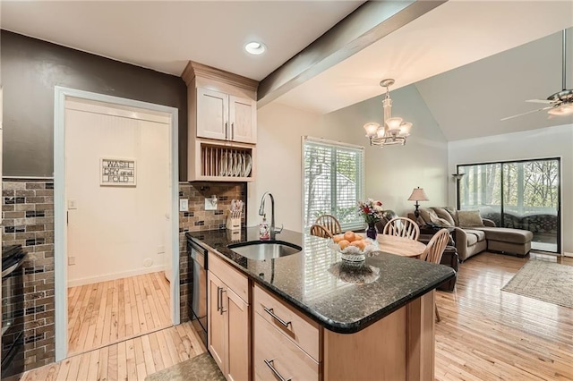 kitchen with dark stone countertops, a sink, decorative backsplash, open floor plan, and light wood-style floors
