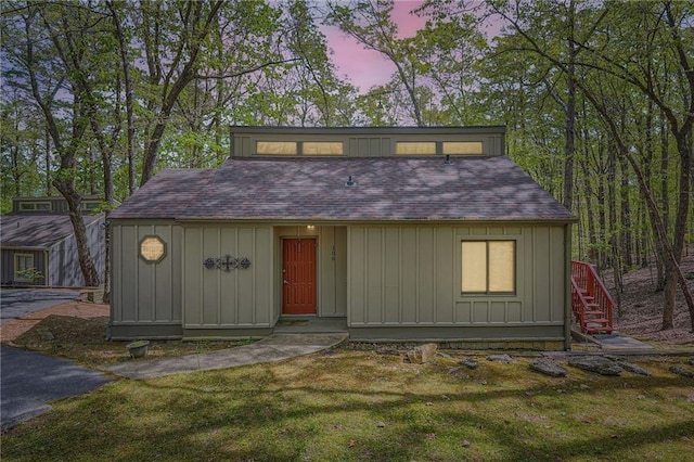 view of front of house featuring board and batten siding, a shingled roof, a front lawn, and stairs