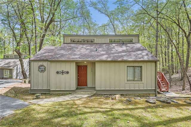 view of front facade featuring board and batten siding, a shingled roof, a front lawn, and stairs