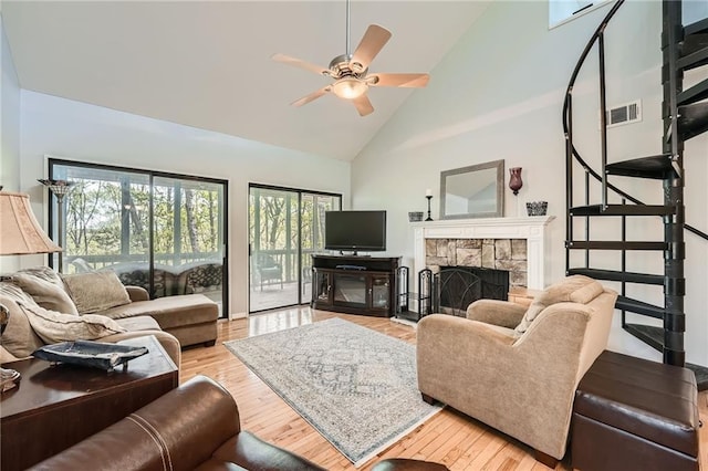 living room with light wood finished floors, a stone fireplace, visible vents, high vaulted ceiling, and ceiling fan