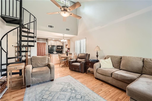 living room featuring stairway, ceiling fan with notable chandelier, light wood-type flooring, a towering ceiling, and visible vents