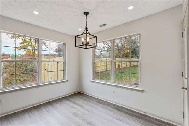 unfurnished dining area with a textured ceiling, a wealth of natural light, wood finished floors, and visible vents