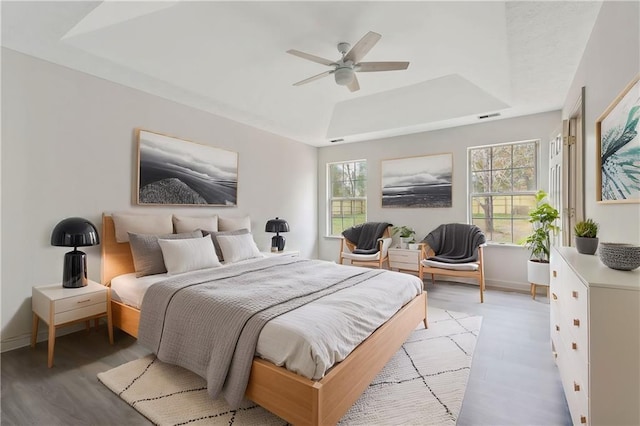 bedroom featuring a tray ceiling, visible vents, ceiling fan, light wood-type flooring, and baseboards