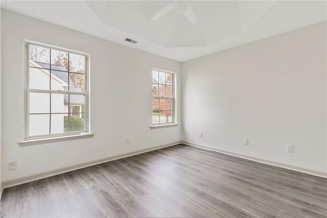 spare room featuring wood finished floors, visible vents, baseboards, a ceiling fan, and a tray ceiling