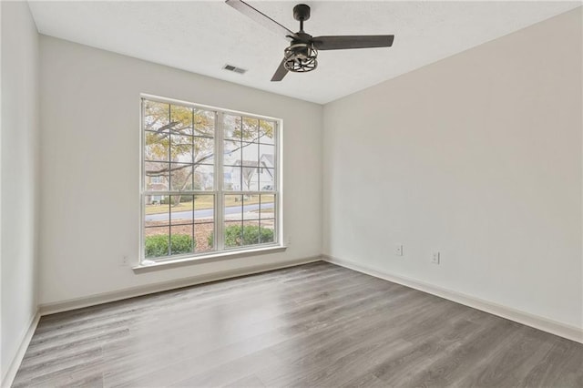 spare room featuring light wood finished floors, a ceiling fan, visible vents, and baseboards