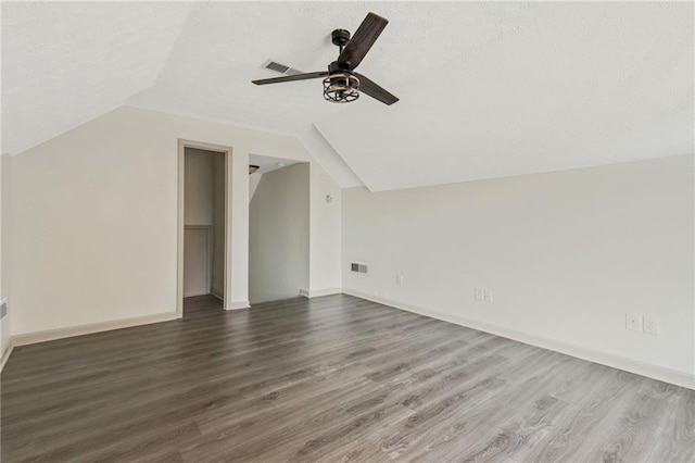 additional living space with a ceiling fan, vaulted ceiling, visible vents, and dark wood finished floors