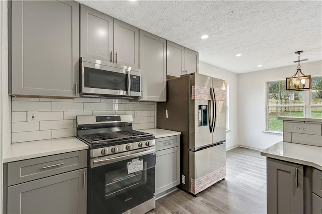 kitchen with light countertops, appliances with stainless steel finishes, gray cabinets, dark wood-style floors, and tasteful backsplash