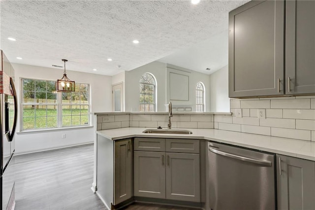 kitchen with gray cabinets, light countertops, decorative backsplash, stainless steel dishwasher, and a sink