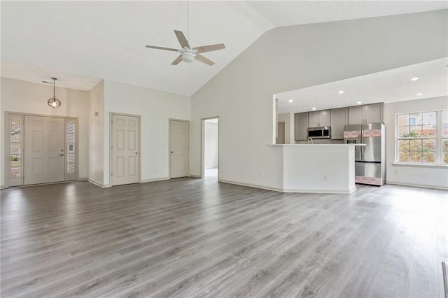 unfurnished living room featuring ceiling fan, high vaulted ceiling, wood finished floors, and baseboards