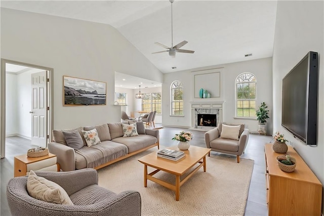 living area featuring a fireplace, visible vents, light wood-style flooring, high vaulted ceiling, and ceiling fan with notable chandelier