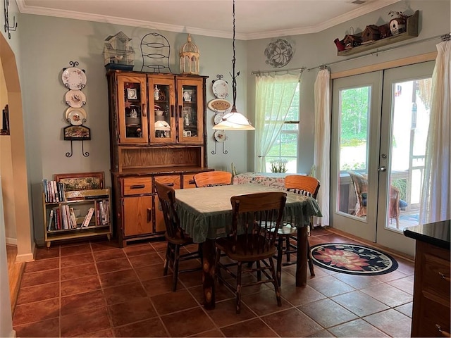 dining space featuring dark tile patterned floors, crown molding, arched walkways, and french doors