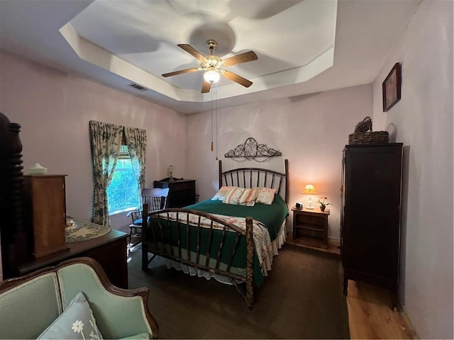 bedroom featuring a raised ceiling, wood finished floors, ceiling fan, and baseboards