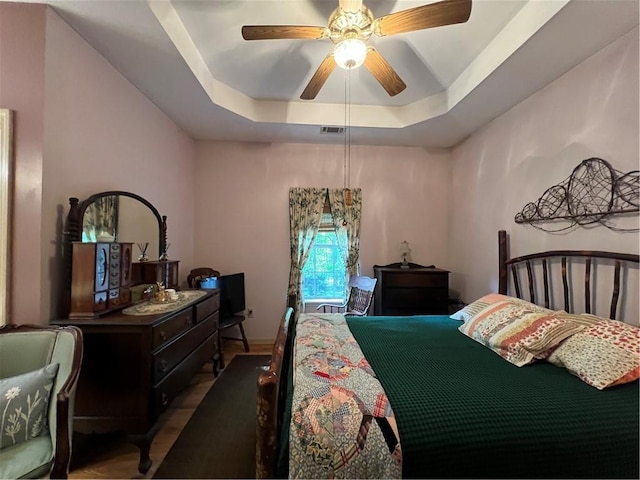 bedroom with a raised ceiling, a ceiling fan, and wood finished floors
