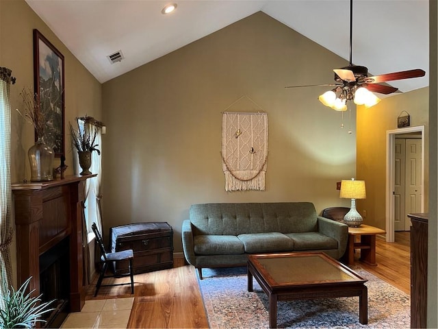 living area with light wood-style flooring, a ceiling fan, a fireplace with flush hearth, high vaulted ceiling, and baseboards