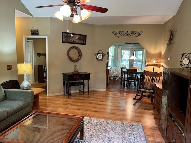 living area with ceiling fan, light wood-style floors, baseboards, and arched walkways